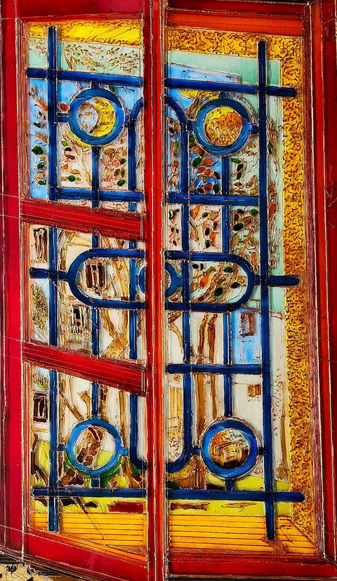 Blue wrought-iron bars and circles lattice a red-framed window, while a sunlit garden and pale stone glow through the panes behind
